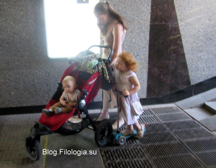 Мама с детской коляской и двумя маленькими  дочками в подземном переходе на ходу говорит по телефону.
